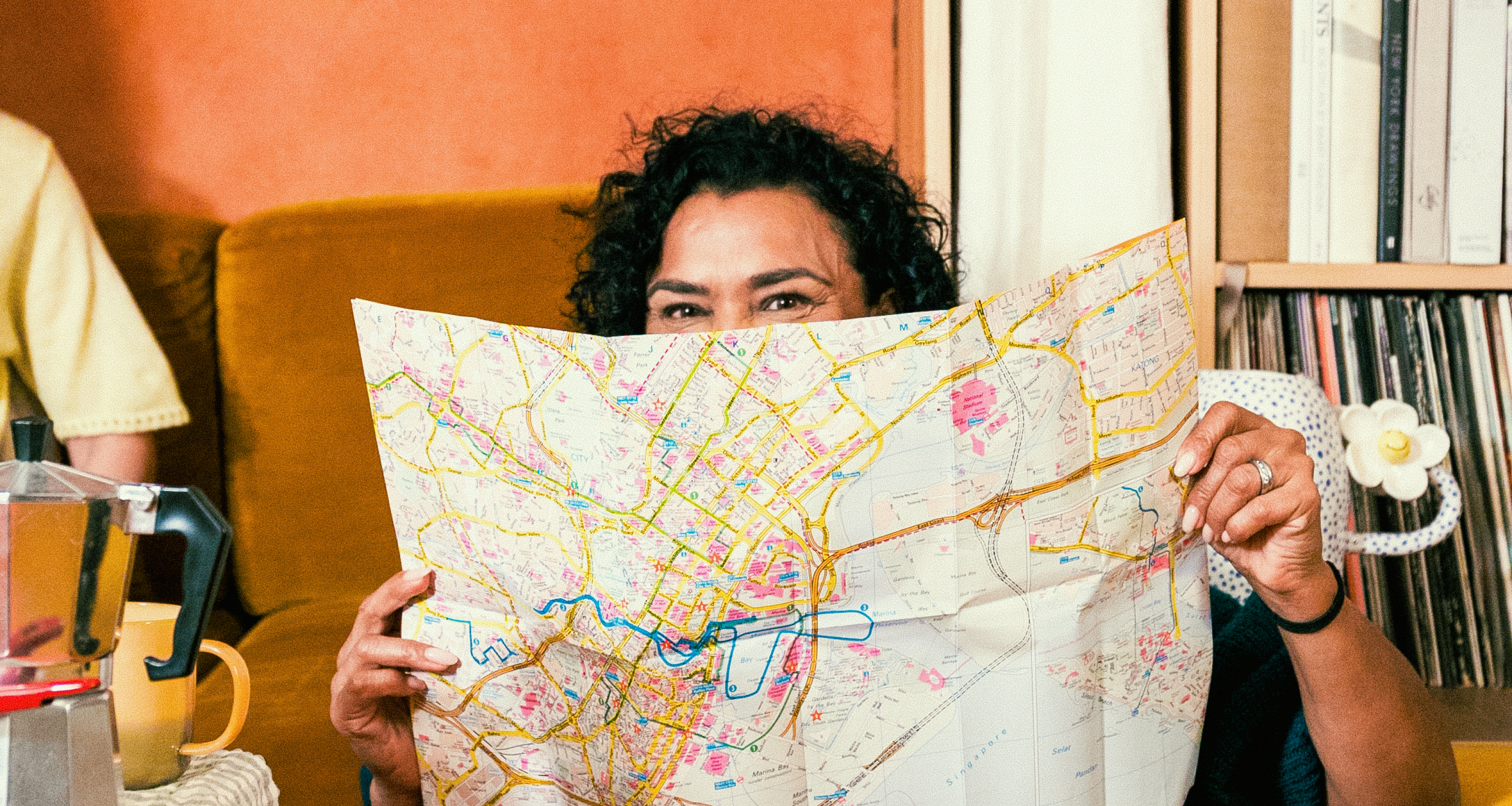 A woman sat facing the camera holding up a map to cover the bottom half of her face.