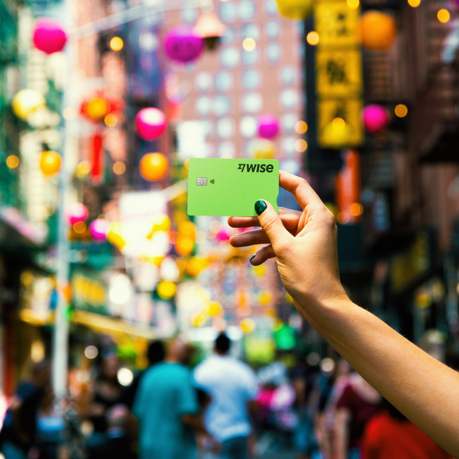 A Wise debit card help up against a colourful, blurred city background.