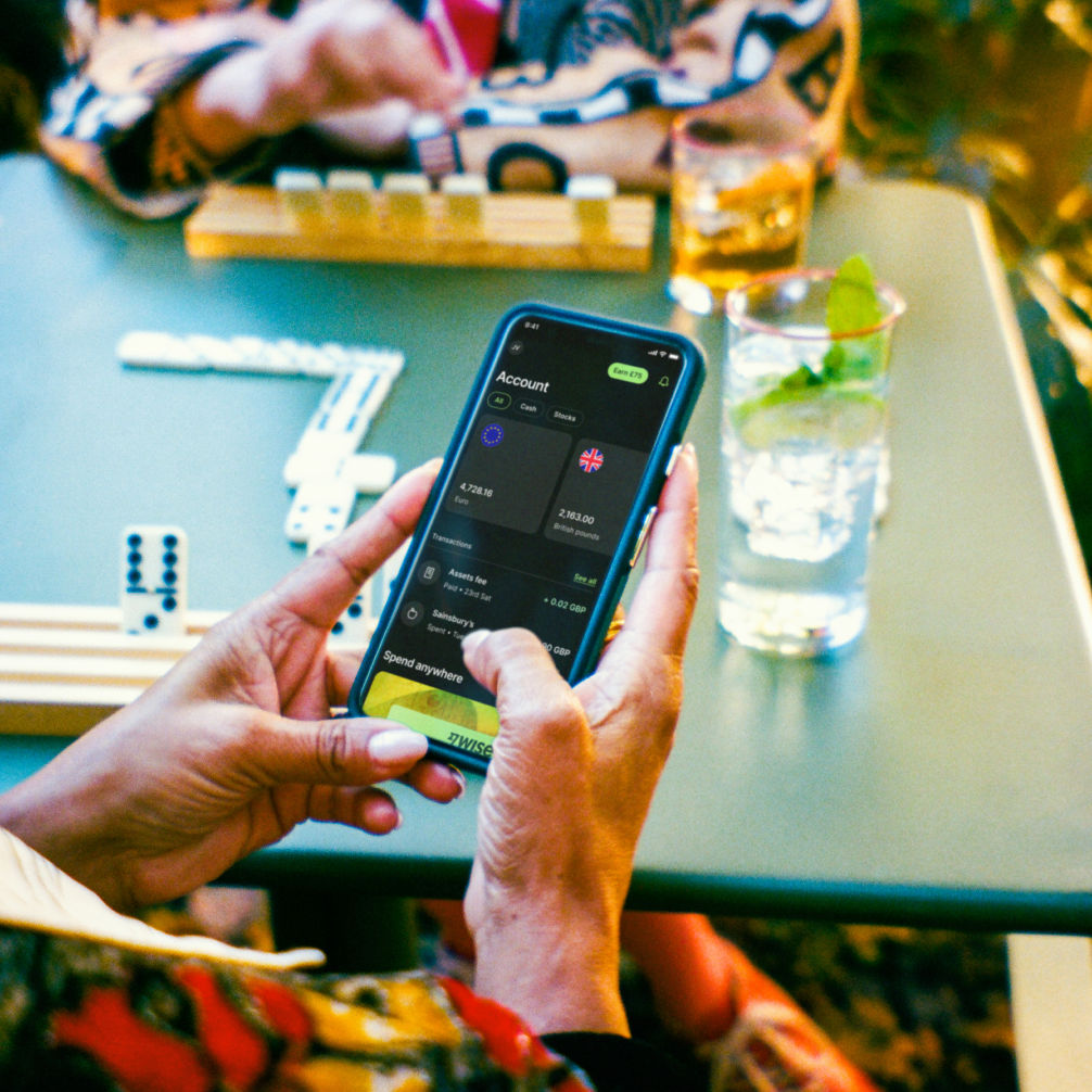 A close up shot of a mobile phone held in someone's hands, with a table in the background.