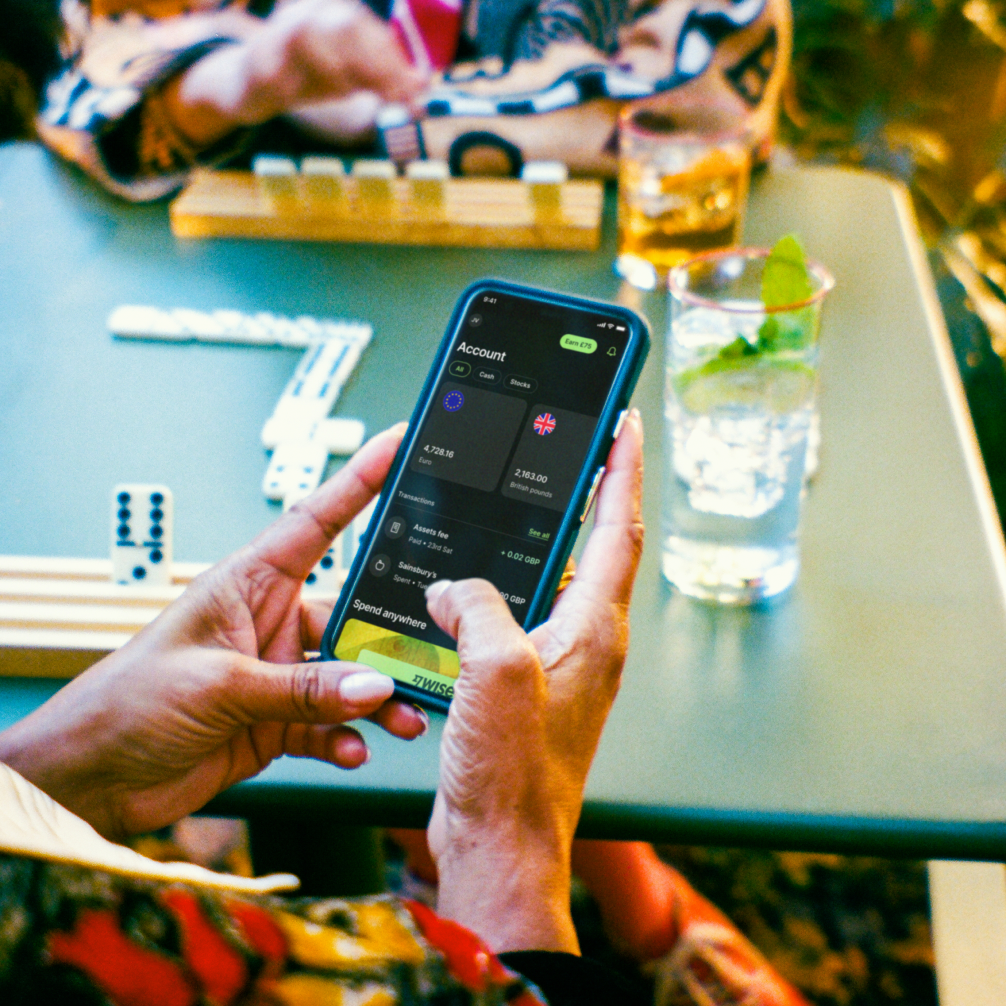 A close up shot of a mobile phone held in someone's hands, with a table in the background.
