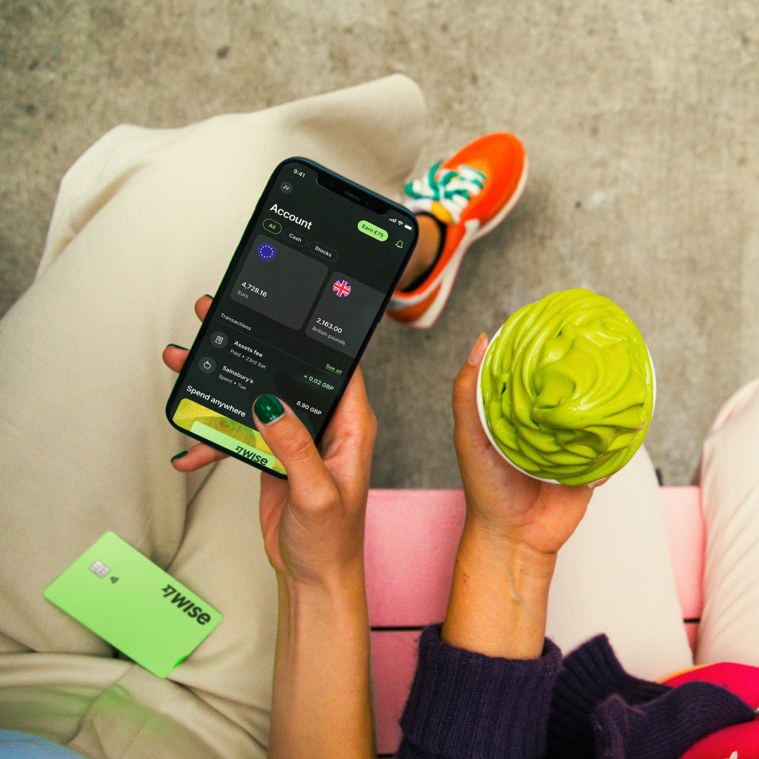 Two people sat on a bench, shot from above, one holding a phone with the Wise app open, another holding an ice cream.